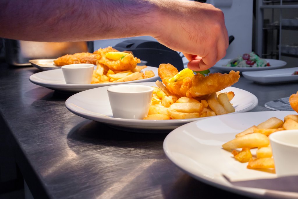 Chef finishing plates of battered fish and chips in a busy kitchen
